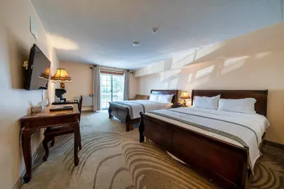 a hotel room with two beds and a desk and a window at Fullerton Manor Inn in Niagara Falls