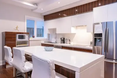 a white kitchen with a large white island with white chairs at Hillcrest Modern House in Toronto