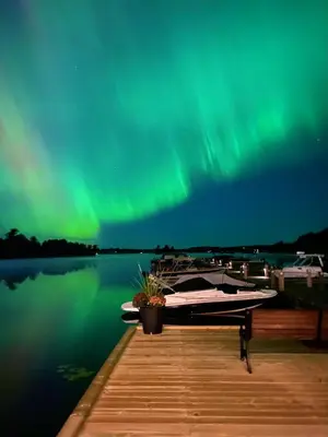 a pier with a boat on the water with the northern lights at Blue Spruce Bed and Breakfast Muskoka in Gravenhurst