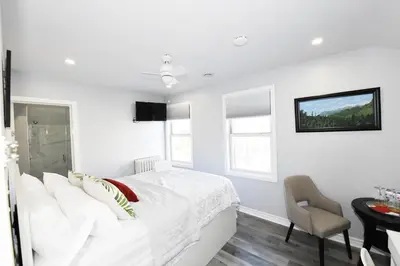a white bedroom with a white bed and a chair at Serene Niagara Inn in Niagara Falls