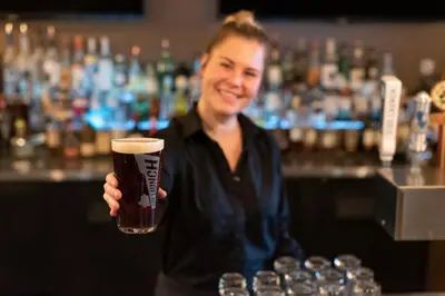 a woman holding a glass of beer in a bar at Georgian Bay Hotel Trademark Collection by Wyndham in Collingwood