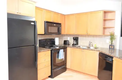 a kitchen with a black refrigerator and wooden cabinets at Bombay Suites Mississauga in Mississauga