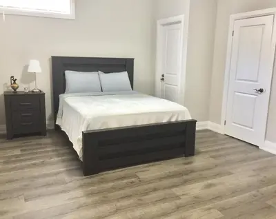 a bedroom with a bed with white sheets and a wooden floor at Charming, Comfortable Bsmt Apartment in Pickering in Pickering
