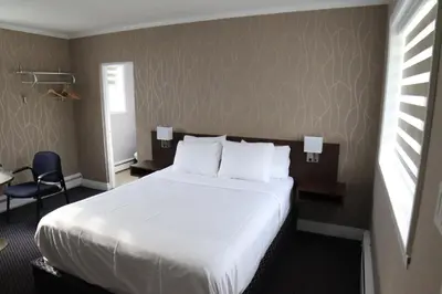 a hotel room with a white bed and a chair at Walkerton Inn Motel in Walkerton