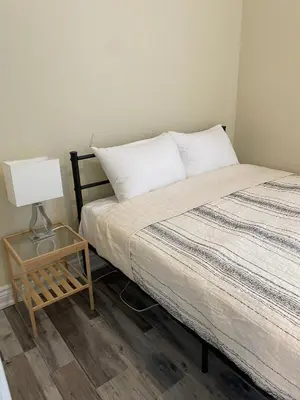a bedroom with a bed and a table with a lamp at Comfortable and Convenient Apartment in Central Niagara in St. Catharines