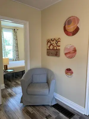 a living room with a chair and paintings on the wall at Comfortable and Convenient Apartment in Central Niagara in St. Catharines