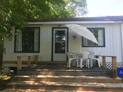 a porch with a table and chairs and an umbrella at Beachside on Lake Muskoka in Port Carling