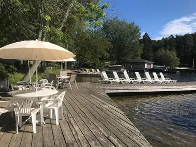 a wooden deck with chairs and tables and an umbrella at Beachside on Lake Muskoka in Port Carling