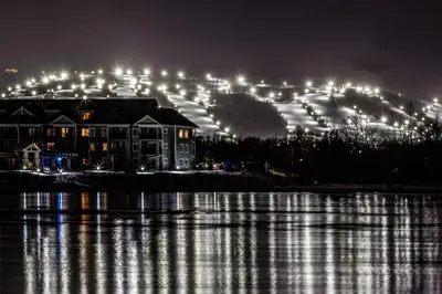 a house with lights on a hill behind a body of water at Condo 413 at North Creek Resort by Vacasa in Blue Mountains