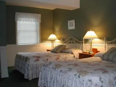 two beds in a bedroom with green walls and two lamps at Canterbury Inn in Niagara on the Lake