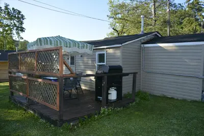 a wooden deck with a grill and a house at Trent River Cottages in Hastings