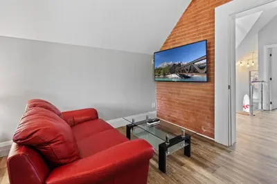 a red couch in a living room with a tv on a brick wall at ENTIRE 1 BEDROOM APARTMENT ACROSS FROM GOOGLE - br5 in Kitchener