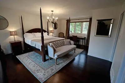 a bedroom with a bed and a chair and a chandelier at Arrowstone Farmhouse in Historic Old Town in Niagara on the Lake