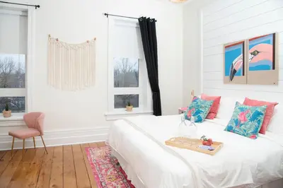 a white bedroom with a bed and a pink chair at The Juniper Inn in St. Catharines