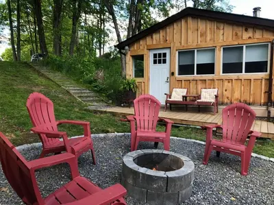 four red chairs and a fire pit in front of a cabin at The hidden nest in Marmora