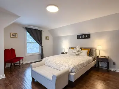 a bedroom with a large bed and a red chair at The Promenade Cottage License # 002-2023 in Niagara on the Lake