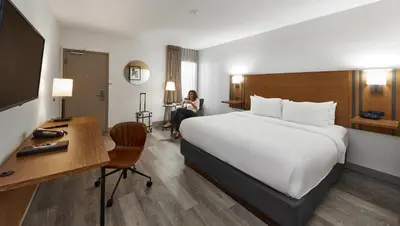 a hotel room with a bed and a woman sitting in a chair at Canadas Best Value Inn Toronto in Toronto