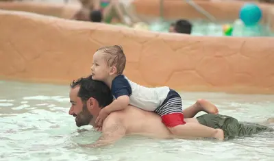 a man holding a child on his back in a swimming pool at Americana Waterpark Resort & Spa in Niagara Falls