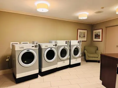 a laundry room with three washing machines and a chair at Best Western Plus Stoneridge Inn & Conference Centre London Ontario in London