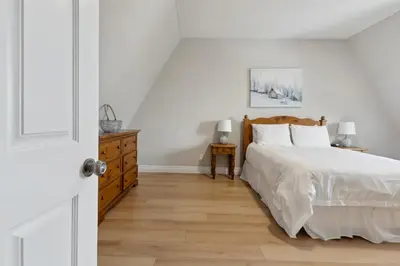 a white bedroom with a bed and a wooden dresser at 3BR Snowbridge Chalet in Blue with Golf Course View in Collingwood