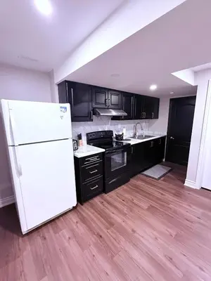 a kitchen with black cabinets and a white refrigerator at Spacious basement in Mississauga