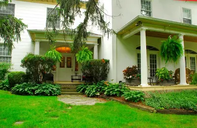 a white house with a porch and green yard at Brockamour Manor Bed and Breakfast in Niagara on the Lake
