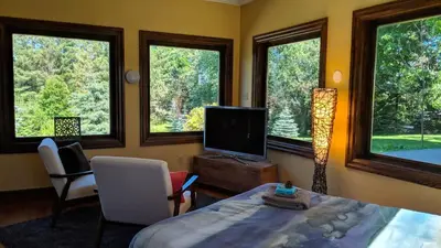 a living room with a tv and a bed and windows at The Front Porch Room of a 140-Year-Old Victorian House in Orangeville