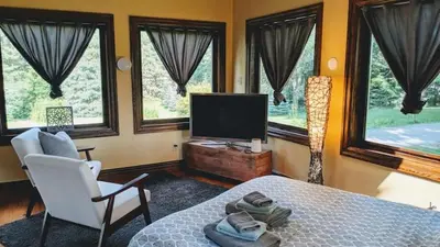 a bedroom with a bed and a tv and windows at The Front Porch Room of a 140-Year-Old Victorian House in Orangeville