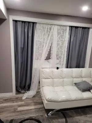a white couch in a living room with curtains at Adorable Studio Basement Suite in South Barrie in Barrie