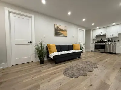 a living room with a black couch and a kitchen at Modern 1BR - Heart of Queen West in Toronto