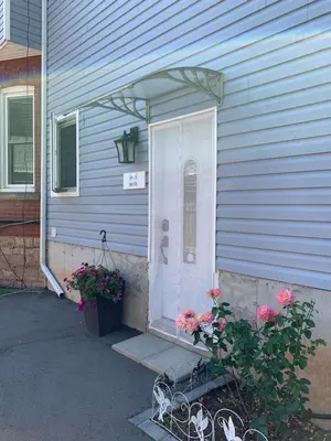a blue house with a white door and flowers at Ambiance by the Falls Cozy Suite in Niagara Falls