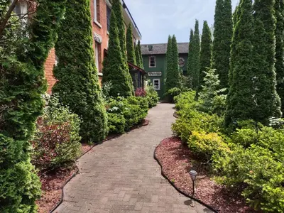 a brick path in a garden with trees and a building at The King George Inn in Cobourg