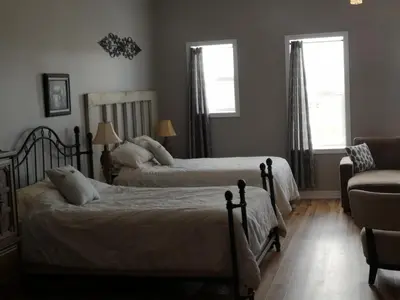 a bedroom with two beds and a chair and two windows at Canalside Restaurant & Inn in Port Colborne