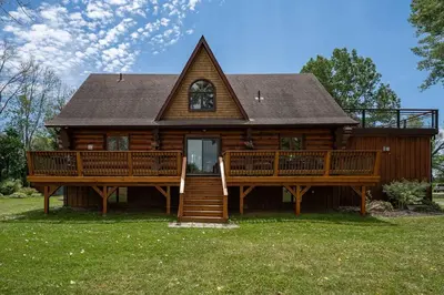 a large wooden house with a large porch and stairs at Unique Log House by the Lake, Retreat with Spa Amenities near Presque'ile Provincial Park in Brighton