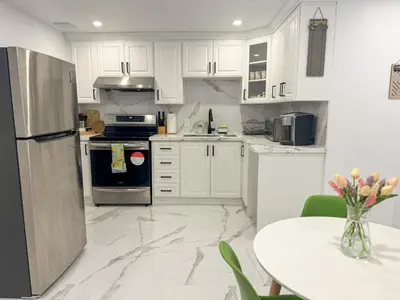 a kitchen with white cabinets and a table and a refrigerator at The Khan Villa in Whitby