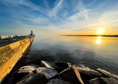 a pier with a lighthouse in the water at sunset at Luxe Lodges on Lake Erie in Port Dover