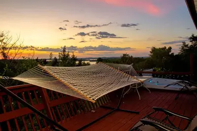 a hammock on a deck with a sunset in the background at Cozy Sunset Cottage Overlooking Rice Lake in Roseneath