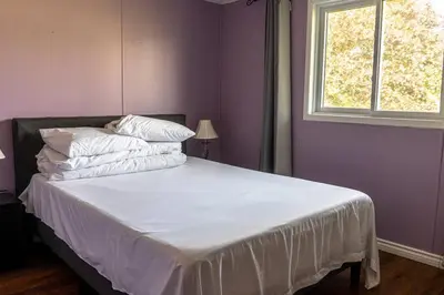 a bedroom with a bed with white sheets and a window at Cozy Sunset Cottage Overlooking Rice Lake in Roseneath