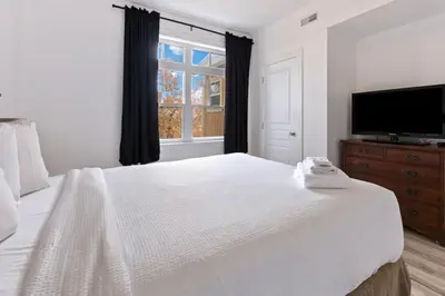 a white bedroom with a large bed and a flat screen tv at Spectacular Rivergrass Chalet Steps to Blue Mtn in Blue Mountains