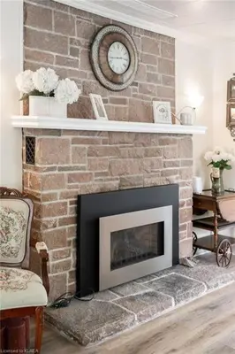 a living room with a brick fireplace with a clock at Pines Bay Waterfront cottage with Hot tub! in Kawartha Lakes