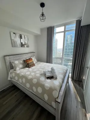 a bedroom with a large bed with a large window at Prestigious 2-Bdrm Condo - across from Scotiabank Arena in Toronto
