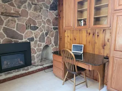 a desk with a laptop on it in a room with a fireplace at Whispering Pines Riverside Retreat in Coboconk