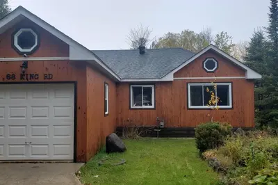 a wooden house with a garage in a yard at Modern Chic Cottage - Hot Tub, Sauna, Tay Trail in Waubaushene